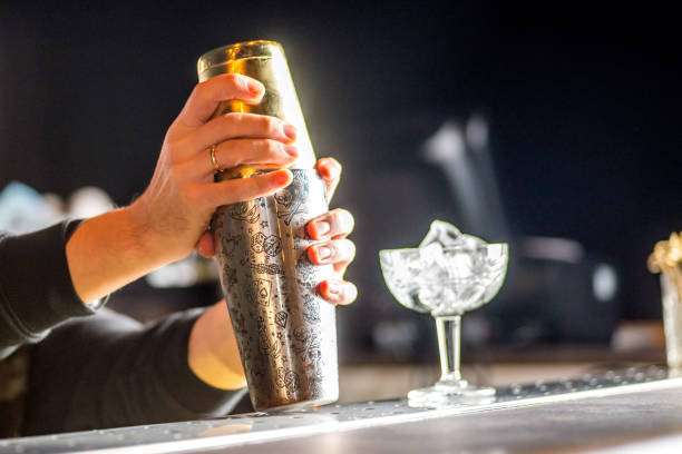 Bartender shaking a cocktail with an ornate metal Cocktail Shaker and ice-filled glass.