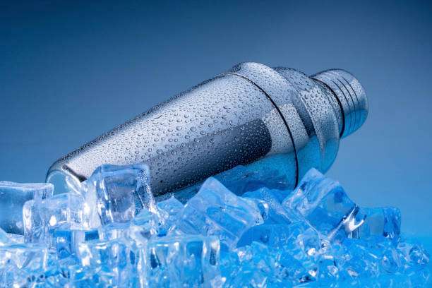 Cold, metallic Cocktail Shaker covered in condensation, resting on blue ice cubes.