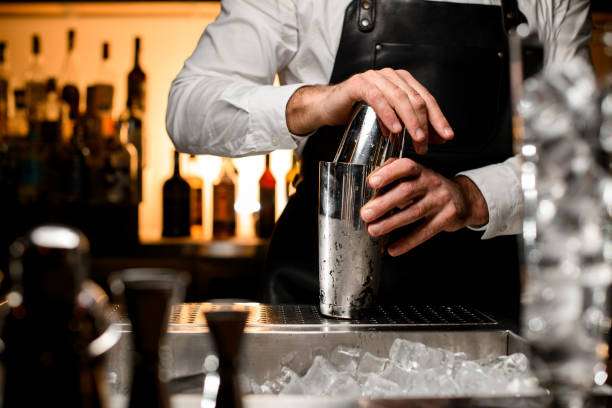 Bartender in apron holding and preparing a professional stainless steel Cocktail Shaker at the bar.