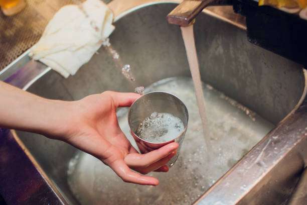 Cocktail shaker cleaning difficulty analysis: Key lies in material and type 3 Hand washing a metal cup, part of a cocktail shaker, under a running faucet.